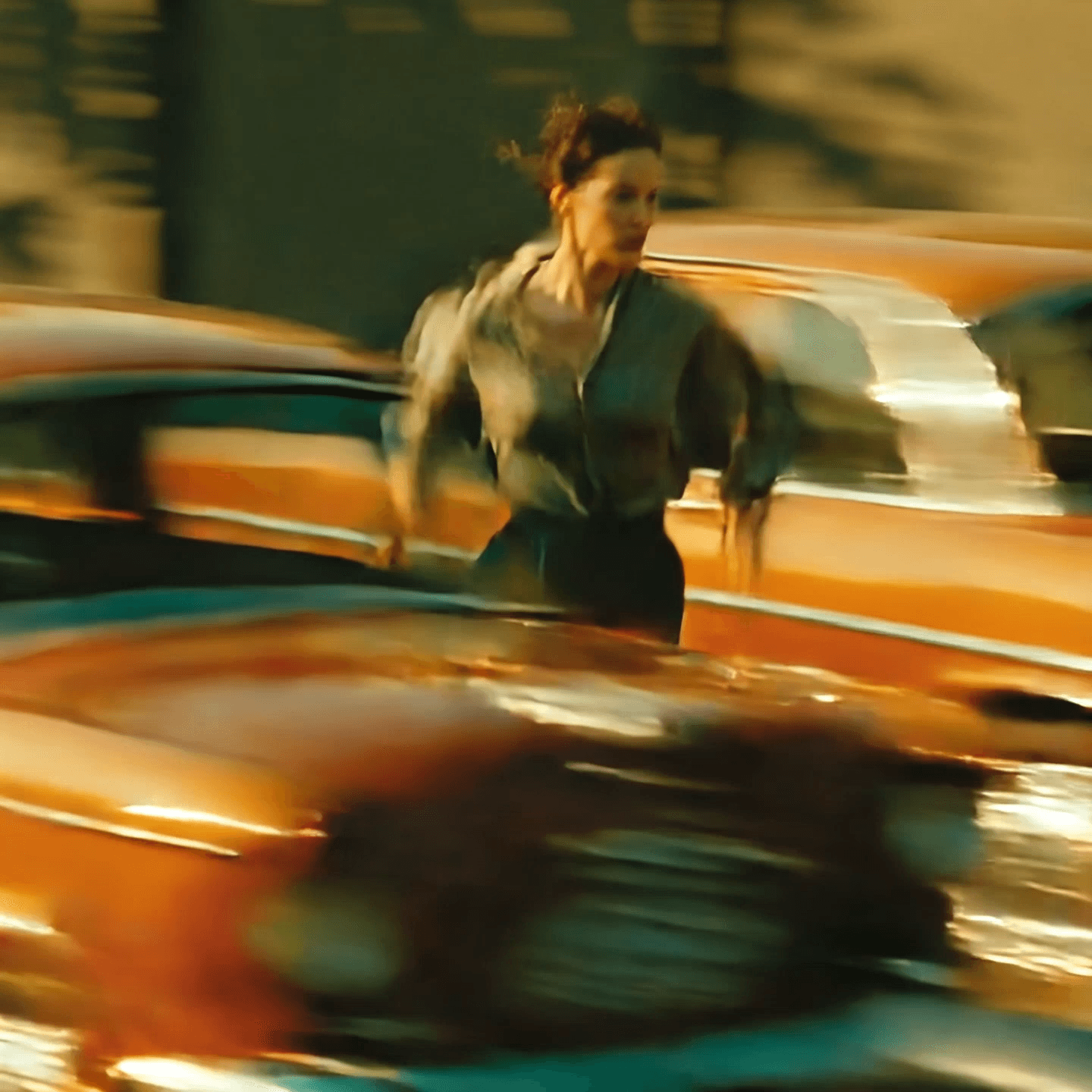 a woman, wearing vintage clothes, navy blue pants and green wide shirt running, surrounded by blurred cars speeding past, motion blur streaks in red, orange, and green tones, captured at low shutter speed, cinematic composition, natural daylight, emotional contrast between stillness and chaos, soft warm lighting, vintage city cars, nostalgic atmosphere, minimalist beige wall in background, expressive body language, realistic urban environment, shallow depth of field, photorealistic, cinematic realism, poetic storytelling in one frame, inspired by fine art photography. Camera Tracking her as she runs